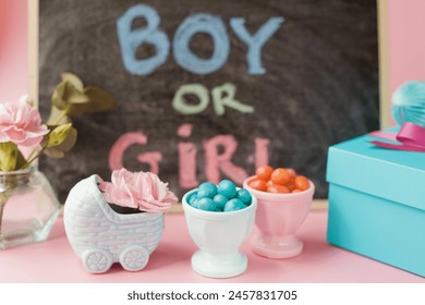 Chalkboard with sign BOY OR GIRL, blue pram vase with pink flowers, blue and pink candies and other decorations. Gender reveal party with pink and blue decorations on a pink background - Powered by Shutterstock