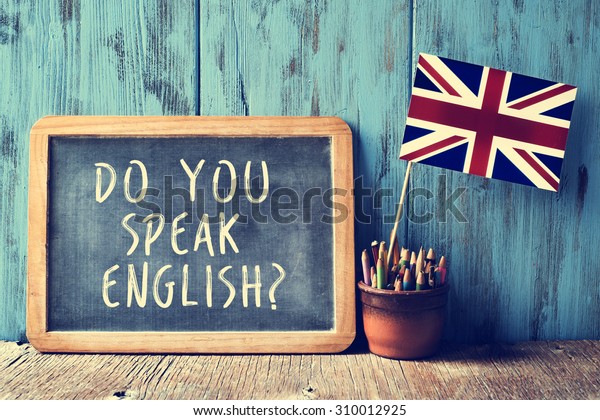 テキストと黒板は英語を話しますか その中に鉛筆とイギリスの国旗の入った鉢と 木の机の上に フィルター効果を持つように書かれている の写真素材 今すぐ編集