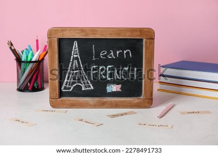 Chalkboard with text LEARN FRENCH, stationery and books on table near pink wall