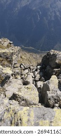 A challenging view looking down a steep, rocky mountain drop-off with a scree slope leading into a deep, hazy valley far below. Concept for risk and verticality.