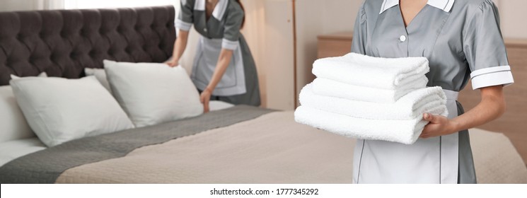 Chambermaid holding stack of fresh towels in hotel room, closeup view with space for text. Banner design