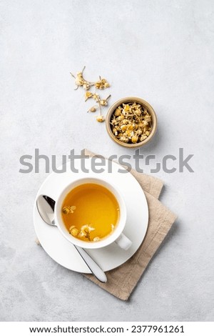 Chamomile herbal tea in a white cup on a light background with dry flowers. The concept of a healthy detox drink for health and sleep. Top view and copy space.