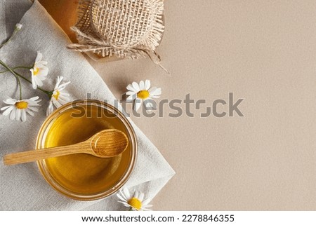 Chamomile syrup in a small bowl and in a jar and chamomile flowers on a linen kitchen towel, topview, copy space
