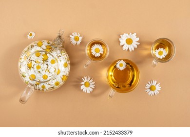 Chamomile Tea. Cups Of Herbal Tea, Transparent Teapot With Camomile Flowers On Brown Background. Calming Drink Concept. Trendy Still Life.