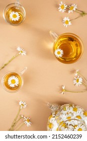 Chamomile tea. Cups of herbal tea, transparent teapot with camomile flowers on brown background. Calming drink concept. Trendy still life.