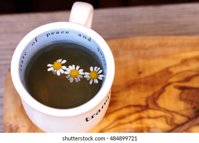 Chamomile Tea With Chamomile Daisy Flowers In A Hot White Cup On A Wooden Rustic Cutting Board And A Spoon. This Home Remedy Is Known To Help Sleep And Aid A Sore Throat