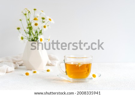 Chamomile tea in a transparent mug with natural small chamomile flowers