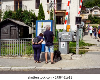 Chamonix, France - Aug 13, 2017: Rear View Of Senior Couple Reading On The Public Tourist Map Their Location In Chamonix Near The Railway Track With Cottages In The Background