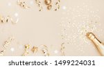 Champagne bottle with confetti stars, holiday decoration and party streamers on gold festive background. Christmas, birthday or wedding concept. Flat lay.