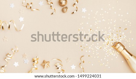 Champagne bottle with confetti stars, holiday decoration and party streamers on gold festive background. Christmas, birthday or wedding concept. Flat lay.