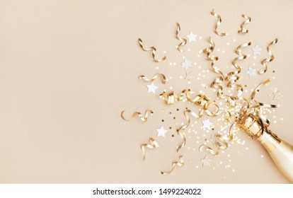 Champagne bottle with confetti stars and party streamers on gold festive background. Christmas, birthday or wedding concept. Flat lay.