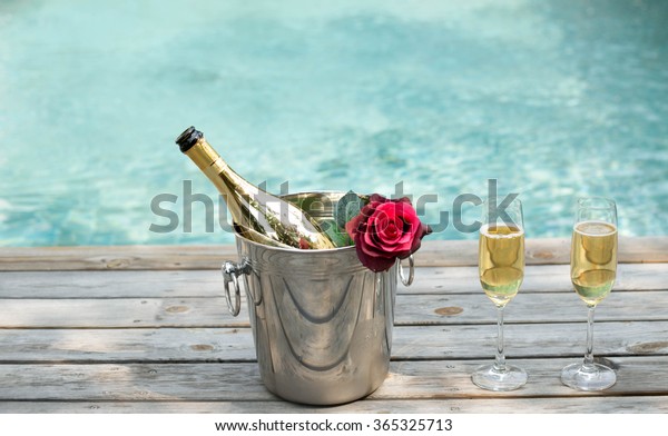 Champagne bottle in ice bucket with flower and\
champagne glass by swimming\
pool