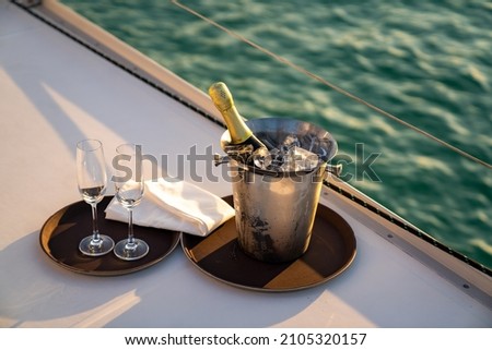 Champagne bottle in ice bucket with champagne glass for serving to passenger tourist on luxury catamaran boat sailing in the ocean at summer sunset. Tropical travel vacation sail yacht trip concept