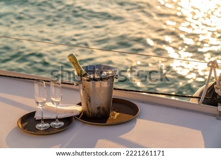 Champagne bottle in ice bucket with champagne glass on the tray for serving to passenger tourist on luxury catamaran boat yacht sailing in the ocean at sunset on summer holiday travel vacation trip.