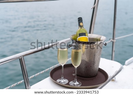 Champagne bottle in ice bucket with champagne glass on the tray for serving to passenger tourist on luxury catamaran boat yacht sailing in the ocean at sunset on summer holiday travel vacation trip.