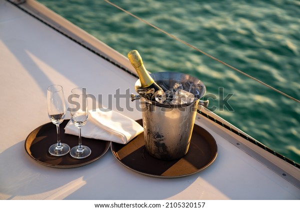 Champagne bottle in ice bucket with champagne\
glass for serving to passenger tourist on luxury catamaran boat\
sailing in the ocean at summer sunset. Tropical travel vacation\
sail yacht trip\
concept