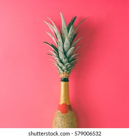 Champagne bottle with pineapple leaves on pink background. Flat lay. Minimal party concept.