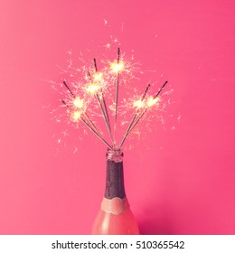 Champagne bottle with sparklers on pink background. Flat lay.