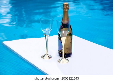 Champagne Bottle And Two Flute Glasses Floating In The Blue Pool Water For Special Date. Couple Celebration Anniversary Concept. Copy Space