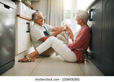 Champagne Celebration, Toast And Senior Couple Having A Drink To Celebrate Retirement On The Floor Of Kitchen In Home. Elderly Man And Woman Happy On Anniversary Of Marriage With Cheers And Alcohol