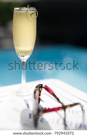 Champagne cocktail by glistening pool in the summer with sunglasses and paper