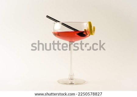 Champagne coupe with pink lady cocktail, lemon twist and black straw isolated on a white background