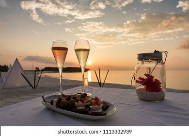 Champagne Glasses And Canapes On A Tropical Beach Setting For Sunset Time