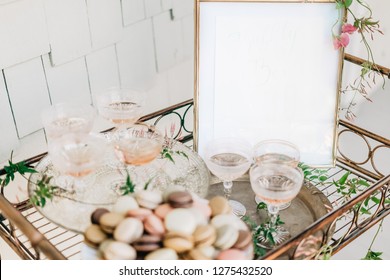 Champagne Glasses And Pastel Macaron Cookies On A Glass Tray On A Gold Drink Cart