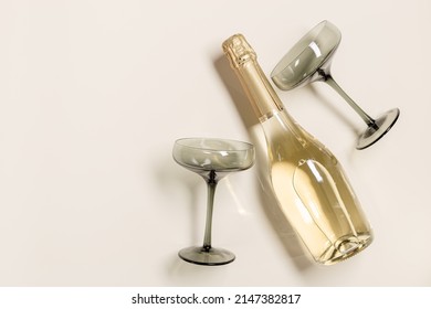 Champagne or sparkling wine bottle, champagne glasses from tinted grey glass on beige background. Festive drink minimal concept. Modern wine glasses, dark colored glass. Creative top view, copy space