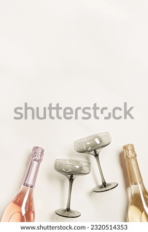 Champagne or sparkling wine bottles with white wine and rose wine, wineglasses grey glass. Romance festive drink concept, glare from sunlight. Stylish colored champagne glasses. Aesthetic flat lay