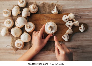 Champignon Mushrooms On A Wood Cutting Board. Woman Cook Slicing Food. Top Down View.