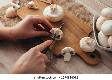 Champignon Mushrooms On A Wood Cutting Board. Woman Cook Slicing Food. Top Down View.