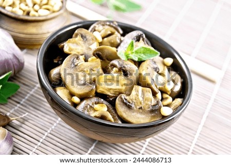 Champignons baked with oregano, wine, garlic, lemon and pine nuts in bowl on background of bamboo napkin