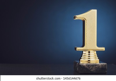 Champion or Winner gold trophy in the shape of a textured 3D number one for 1st place over blue with copy space