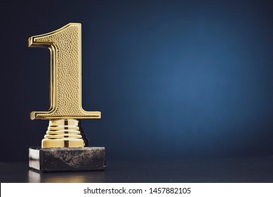 Champion or Winner gold trophy in the shape of a textured 3D number one for 1st place over blue with copy space
