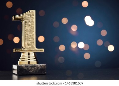 Champion or Winner gold trophy in the shape of a textured 3D number one for 1st place over blue with copy space and bokeh