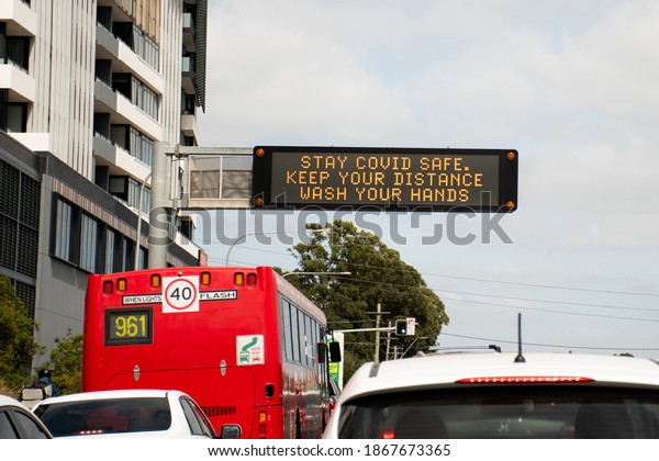Changeable electronic dynamic road sign reads -Stay\
COVID safe. Keep your distance. Wash your hands- on a busy city\
street. Coronavirus\
alert
