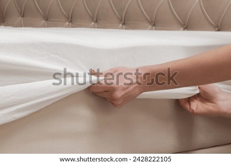 Changing bed sheets. Woman is putting on a fitted white cotton sheet on a mattress while making the bed.	