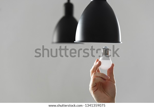 Changing the bulb for led bulb in floor lamp\
in black colour. On light gray\
background.