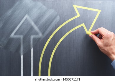 Changing business management concept. Businessman erasing white arrow and drawing yellow arrow on chalkboard.