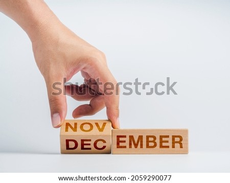 Changing to the last month of the year. The hand is flipping wooden cube blocks for change words, months from November to December on the desk on white background, clean, modern, and minimal style.