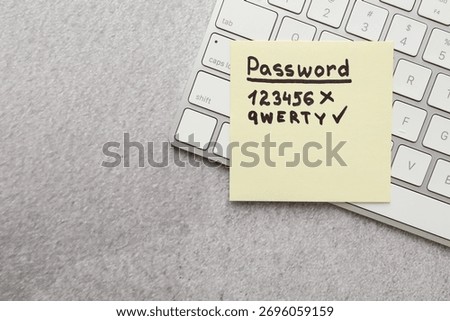Changing password. Sticky note with weak and strong passcodes near computer keyboard on grey table, top view. Space for text