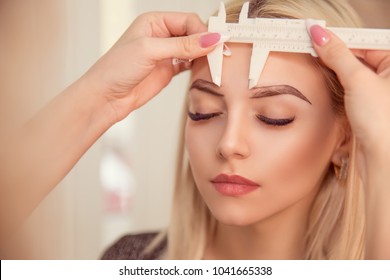 Changing The Shape Of The Brows. Stylist Measuring The Eyebrows With The Ruler. Micropigmentation Work Flow In A Beauty Salon. Woman Having Her Eye Brows Tinted With Semi-permanent Makeup.