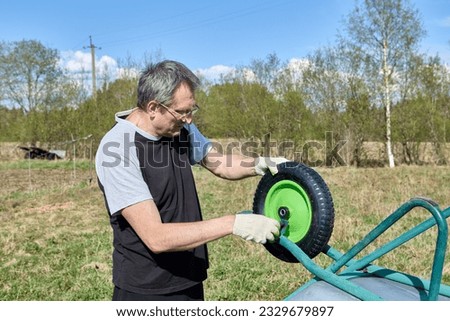 Changing wheel on a garden wheelbarrow, an elderly farmer repairs garden tools.