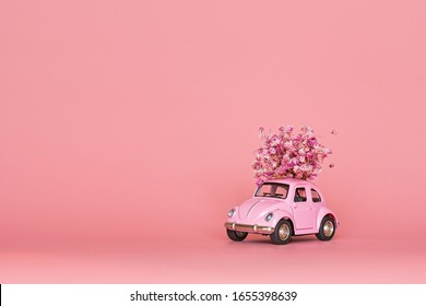 Changxing, China - October 15, 2019: Pink retro toy car delivering bouquet of flowers on pink background. Valentine day, February 14 card. International women day 8 March, mother day, birthday gift