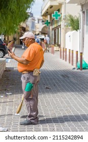 Chania, Crete, Greece - October 1, 2021 Greek Man, Road Sweeper, Caretaker Cleaning City Street Service, During His Break With Cellphone, Phone Call 