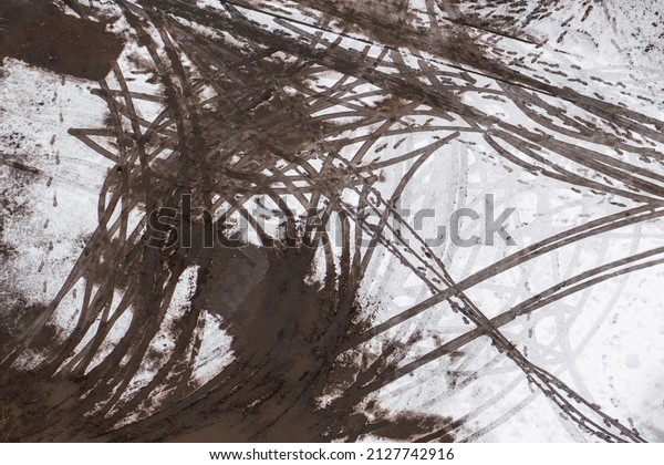 Chaotic traces of\
car tires and human feet on the muddy ground along with a little\
snow. Close up view from\
above.