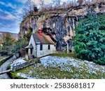 Chapel nestled between cliffs surrounded by trees under blue sky