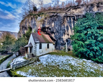 Chapel nestled between cliffs surrounded by trees under blue sky
