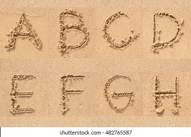 character A B C C E F G H  handwritten on sand.